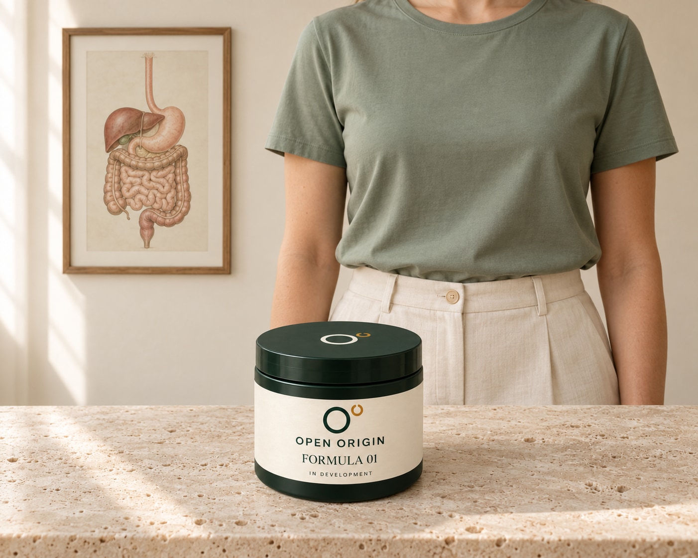 Open Origin concept jar in front of a person’s sage-shirted torso, beside a complete framed digestive-anatomy illustration.